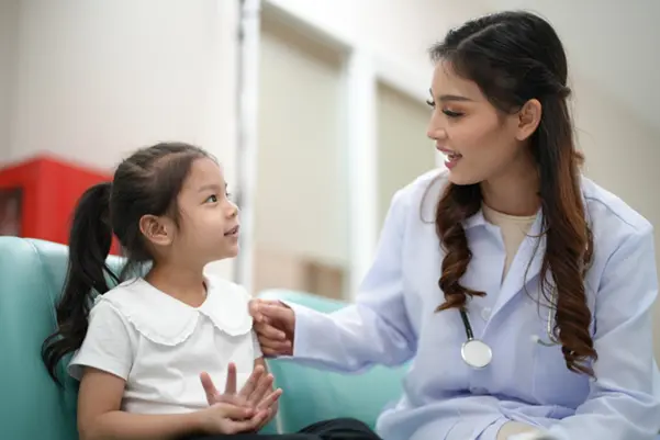 A friendly female paediatric ENT specialist speaking kindly with a young girl during a consultation at the clinic. A friendly female paediatric ENT specialist speaking kindly with a young girl during a consultation at the clinic.