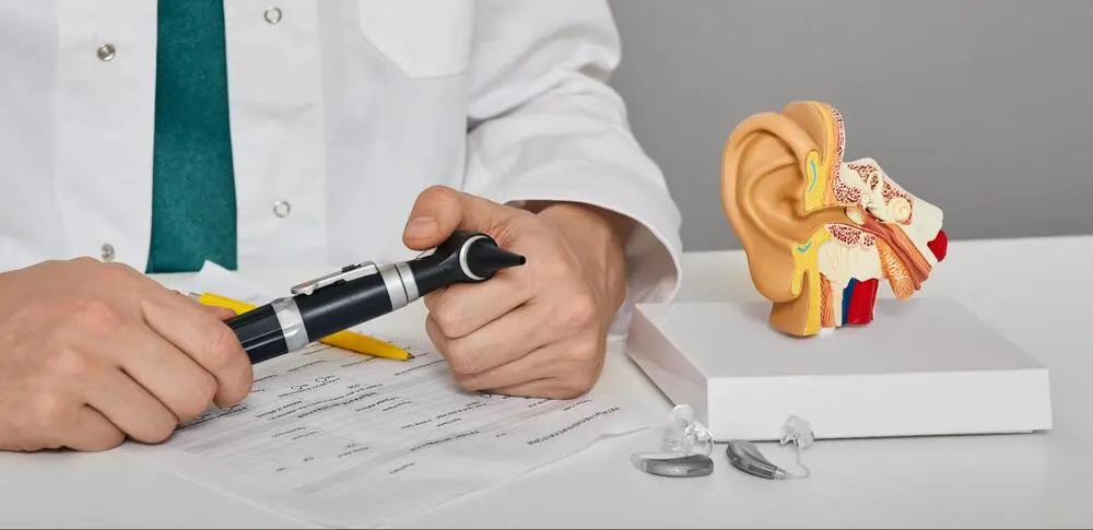 ENT surgeon demonstrating cochlear implant placement A doctor holding an anatomical ear model and a cochlear implant device to explain the surgical procedure.