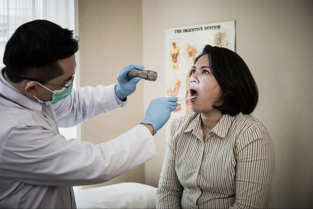 A doctor is using a flashlight and tongue depressor to examine a patient's throat and mouth in an ENT clinic ENT Diagnostic Tools and Examination