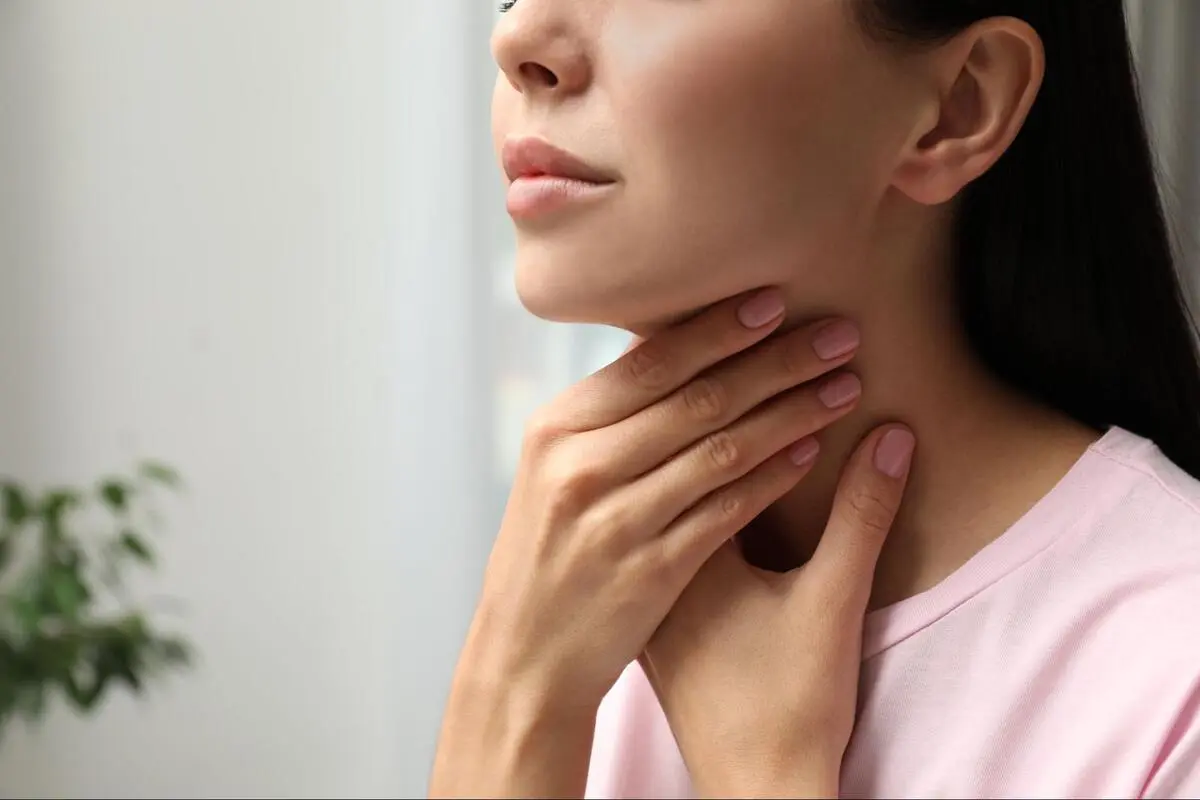 Checking for Early Signs of Thyroid Cancer A young woman touching her neck to check for a painless lump or swelling, a common sign of thyroid cancer.
