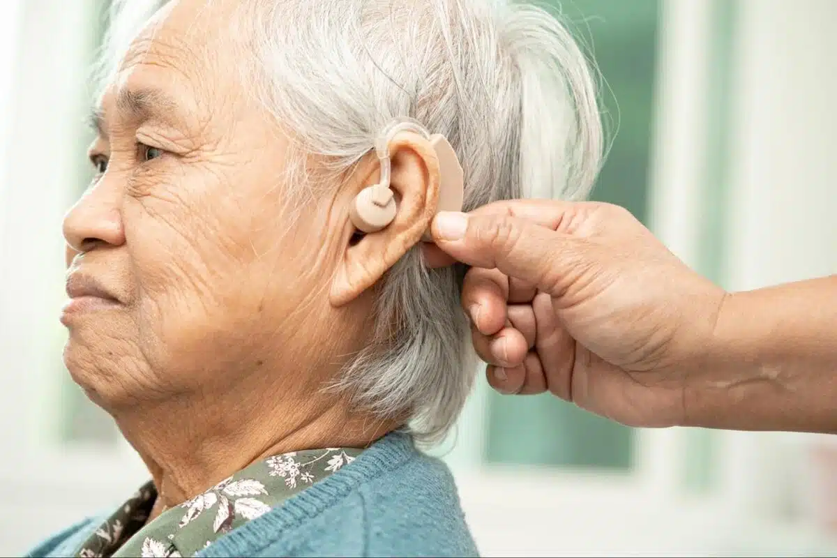 Hearing Aid Fitting for Elderly Patient ENT Care Elderly woman having a hearing aid fitted behind her ear by a caregiver, representing hearing care and ENT support for older adults
