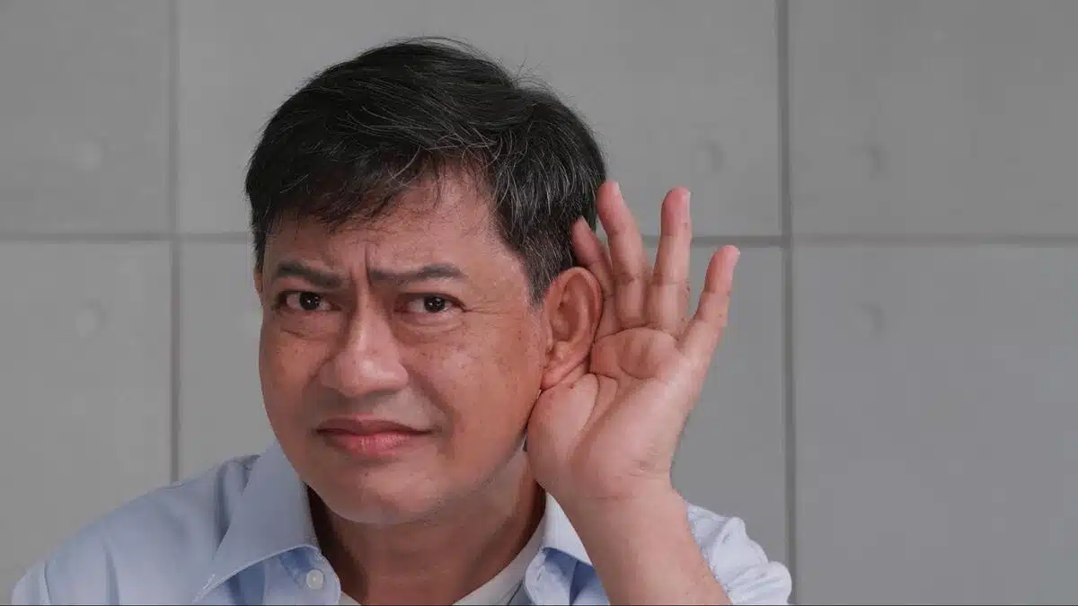 Man Experiencing Hearing Difficulty Middle-aged man cupping his hand to his ear with a concerned expression, representing difficulty hearing and the need to see an ear specialist