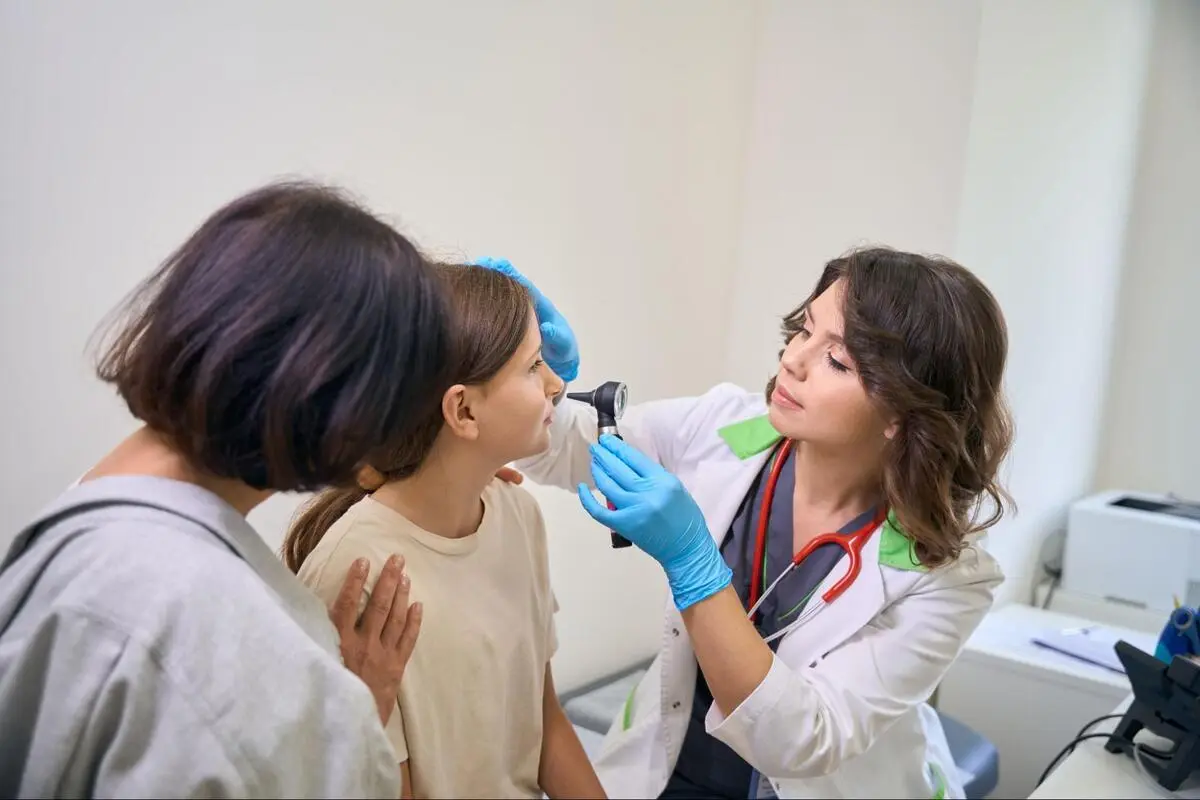 General Practitioner Examining Child's Ear General practitioner using an otoscope to examine a child's ear with the parent present in a clinic