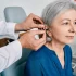 An ENT specialist fitting a hearing aid into the ear of a patient