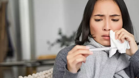 Ill korean woman looking at thermometer with concerned face, catching cold, having fever, having covid, staying at home on sick leave.