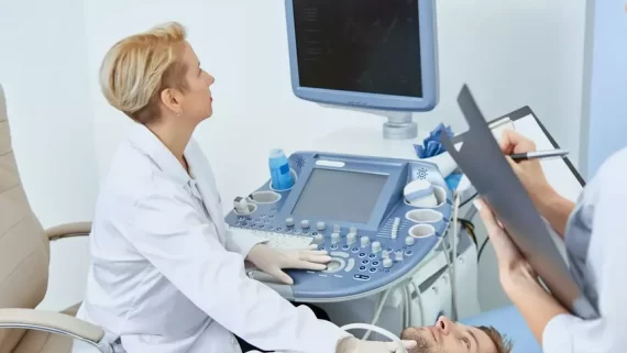 Young man laying on bed during observation on medical concultation in private clinic. Professional doctor good spesialist treating patient with medical equipment with help of young nurse.