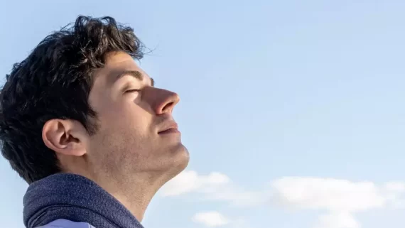Portrait of young boy with head to the sky and eyes closed on a clear day with blue sky and some white cloud